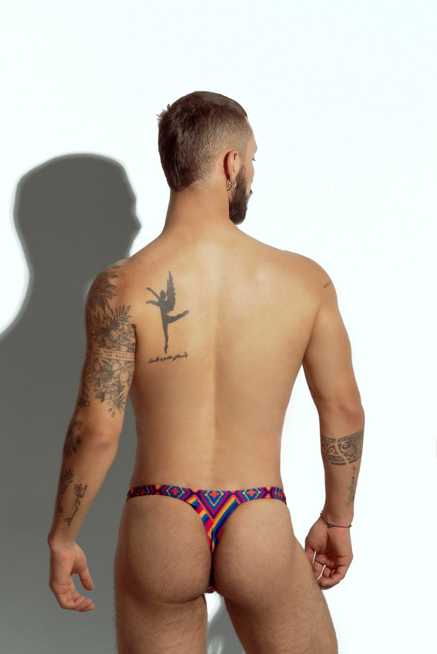 Men's swim thong with vibrant rainbow stripe pattern, designed for gay men looking for bold and colorful beachwear