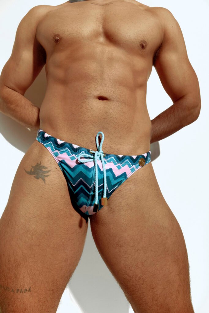 Men's thong swimwear with vibrant chevron pattern in pink, blue, and teal, designed for the gay community