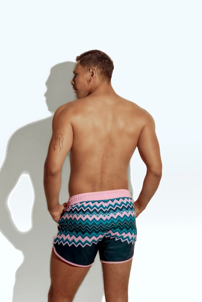 Men's swim short with vibrant chevron pattern in pink, blue, and teal, designed for the gay community