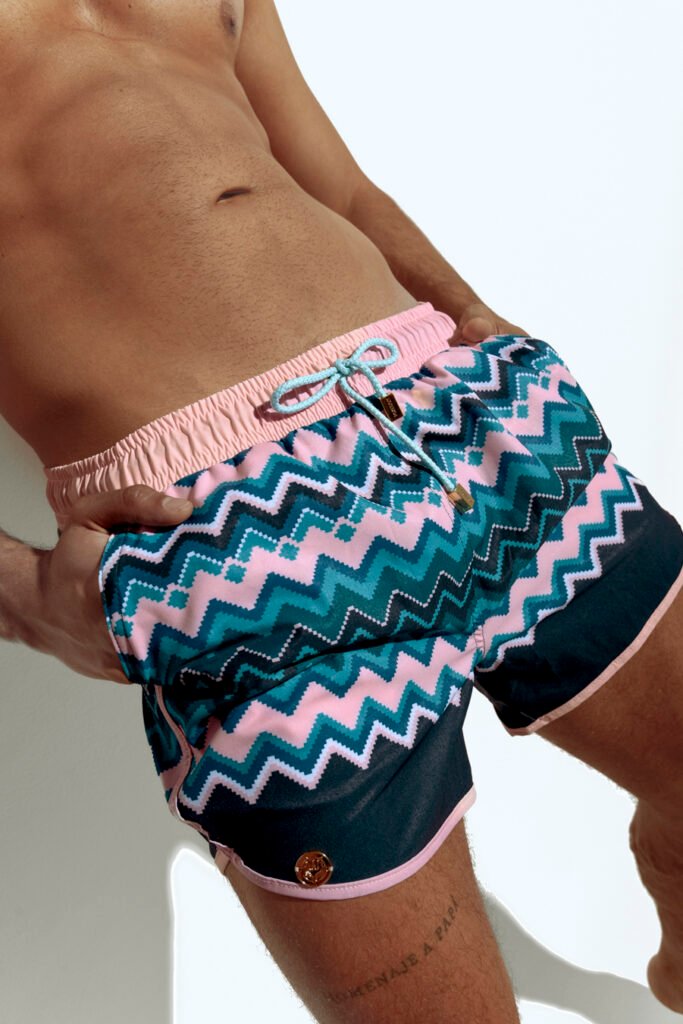 Men's swim short with vibrant chevron pattern in pink, blue, and teal, designed for the gay community